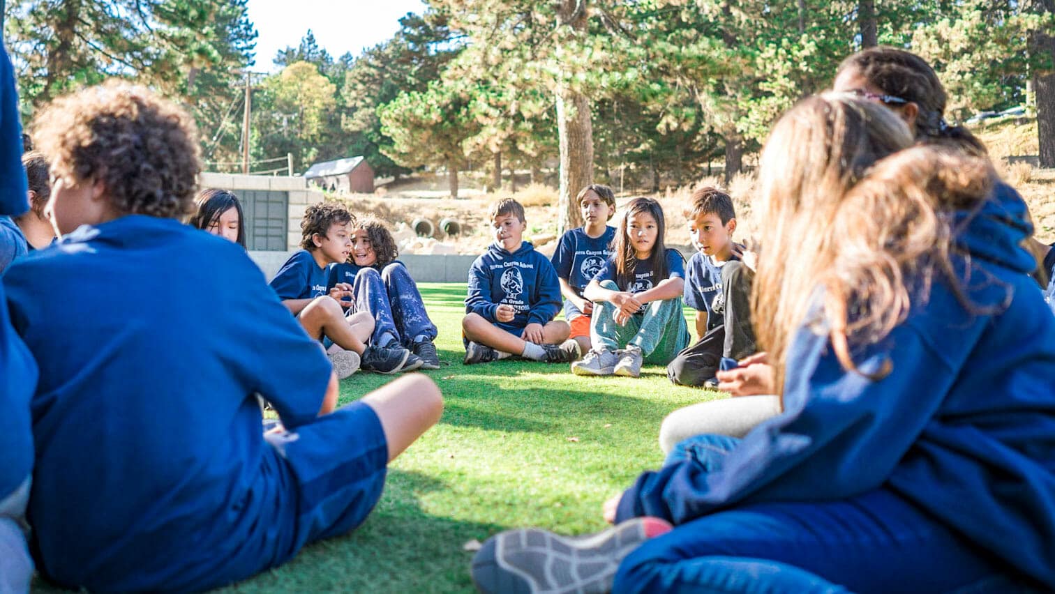 Pali students wearing blue shirts sit on grass outside