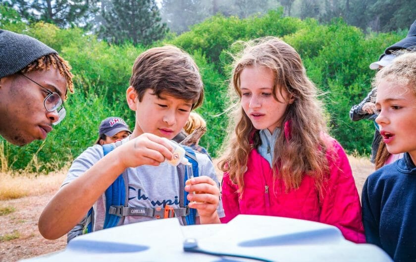 Student pours liquid into vial during outdoors Pali class