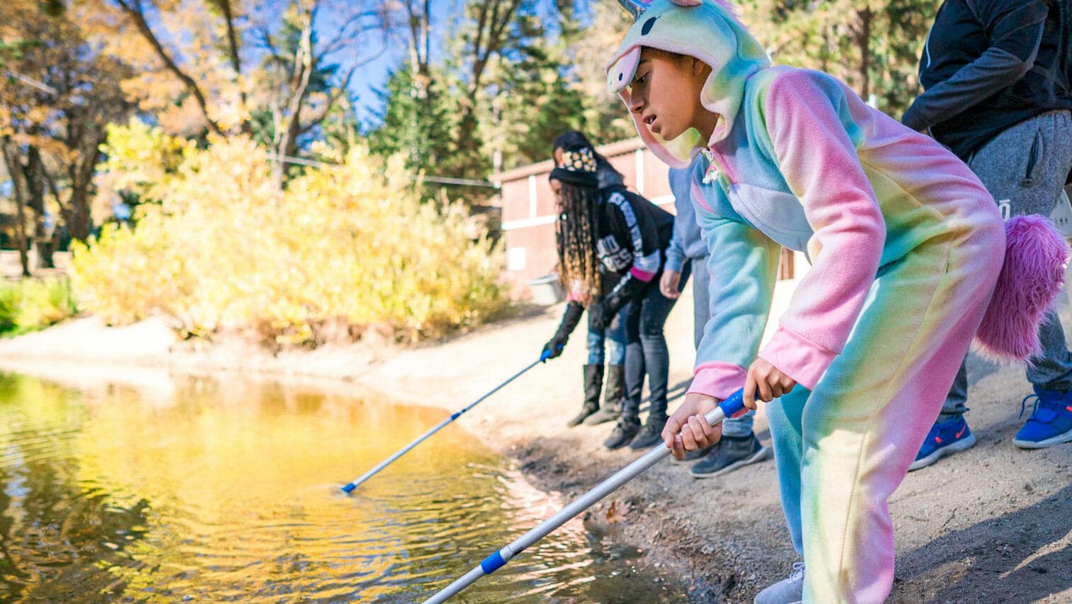 Student in unicorn onesie stands with group to catch frogs in pond